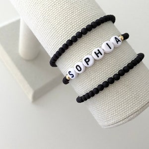 Könnte beinhalten: Drei schwarze Perlenarmbänder, eines mit weißen Perlen, die den Namen "Sophia" buchstabieren.