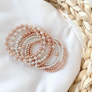 May include: A set of silver and rose gold beaded bracelets stacked together. The bracelets are made of small, round beads and are arranged in a circular pattern.