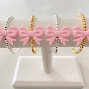 May include: Four bracelets with pink bow charms. Two bracelets are silver and two are gold.