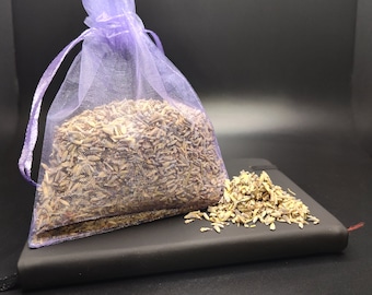 May include: A purple mesh bag filled with dried lavender buds. The bag is sitting on a black notebook with some lavender buds scattered around it.