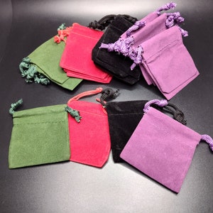 Peut inclure: Plusieurs petits pochons carrés à cordon de serrage de différentes couleurs : vert, rouge, noir et violet. Chaque pochette est dotée d'un cordon de serrage assorti. Les pochons sont fabriqués dans une matière douce semblable à du daim.