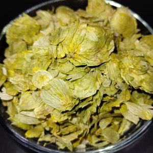 Op de afbeelding: Een close-up van een kom gevuld met gedroogde groene hopbloemen. De hop is lichtgroen van kleur met een lichtgele tint. De hop wordt gebruikt bij het brouwen van bier.