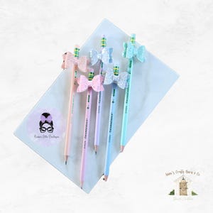 May include: Five pencils with glitter bows attached to the top. The bows are in shades of pink, blue, and green. The pencils are all yellow and have the text "Dixon Ticonderoga" printed on them.