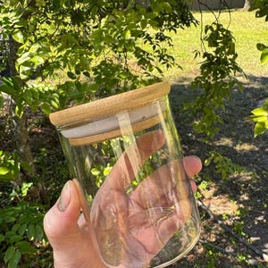 May include: A clear glass jar with a wooden lid. The jar is empty and has a smooth, rounded bottom.