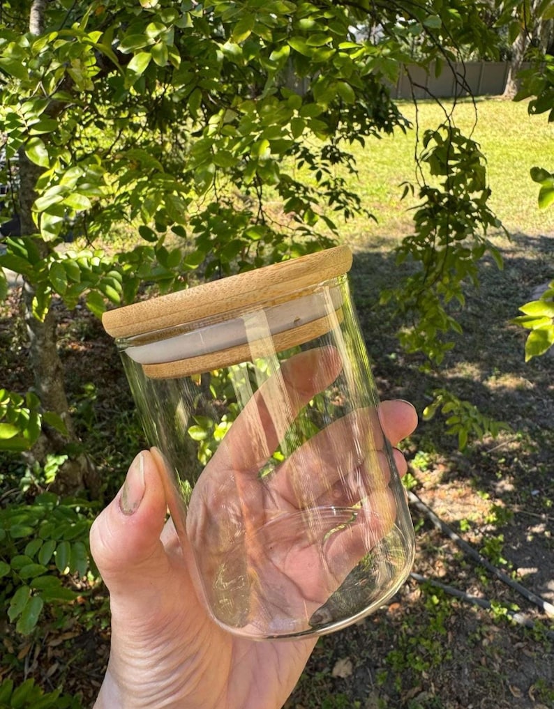 May include: A clear glass jar with a wooden lid. The jar is empty and has a smooth, rounded bottom.