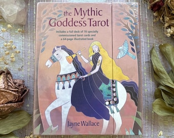 May include: The Mythic Goddess Tarot deck features a pink cover with an illustration of a woman riding a white horse. The deck includes 78 tarot cards and a 64-page illustrated book. The author's name, Jayne Wallace, is printed at the bottom.