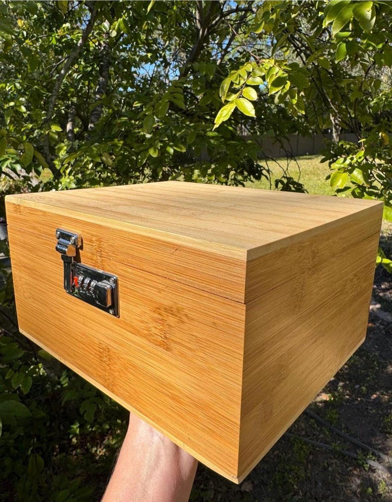 May include: A wooden box with a combination lock. The box is made of light brown wood and has a natural finish. The lock is silver and has a combination dial.