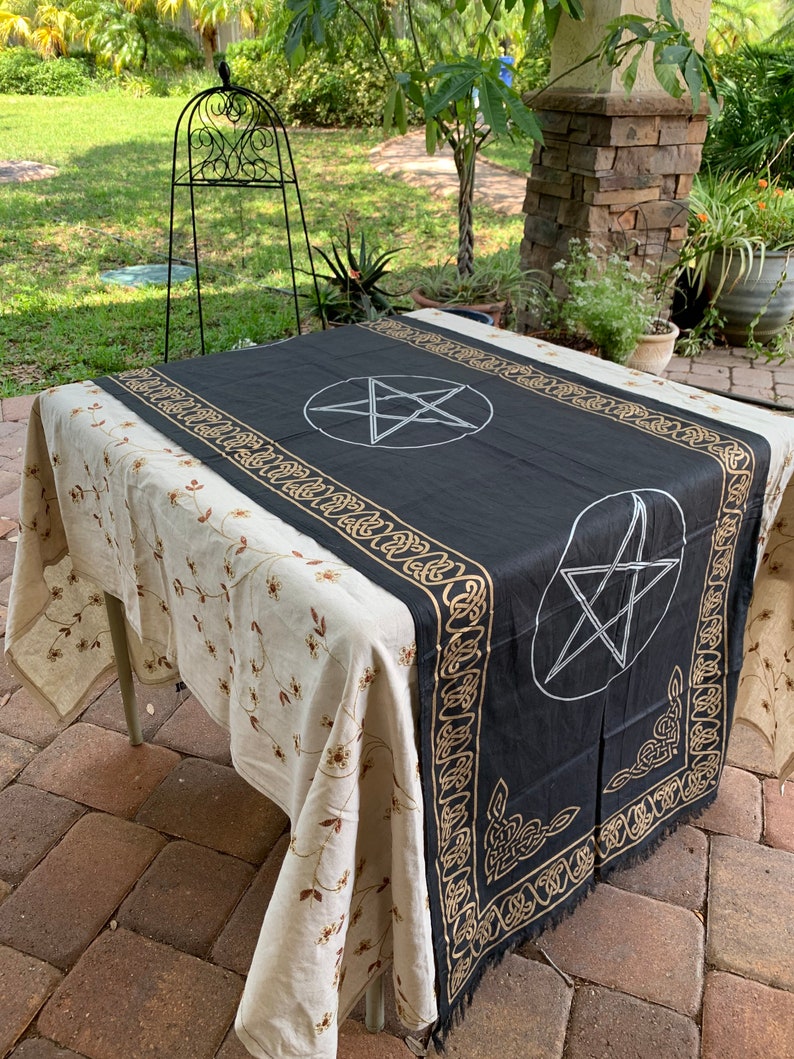 May include: Black altar cloth with gold trim and a white pentagram design. The cloth is laid out on a table with a floral pattern tablecloth.
