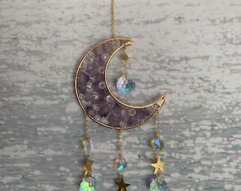May include: A gold wire crescent moon with amethyst crystals and iridescent crystal drops hanging from it. The moon is suspended from a gold chain.