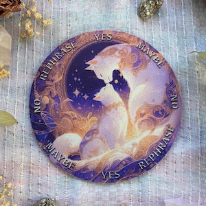 May include: A round, purple and gold divination card featuring two white cats in a loving embrace. The card has the words "YES", "MAYBE", "NO", and "REPHRASE" around the edge, with a starry night sky background.