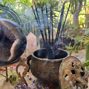 May include: A bronze incense burner with a lid and intricate carvings. The burner is filled with incense sticks that are smoldering and releasing smoke.