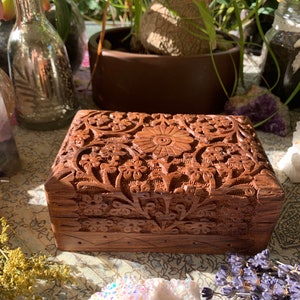 May include: A wooden box with intricate floral carvings. The box is made of dark brown wood and has a rectangular shape. The carvings are detailed and cover the entire surface of the box.