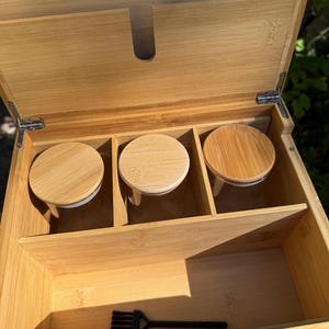 May include: A wooden box with a hinged lid, containing three small glass jars with wooden lids. The box has a small compartment for a brush, which is included.