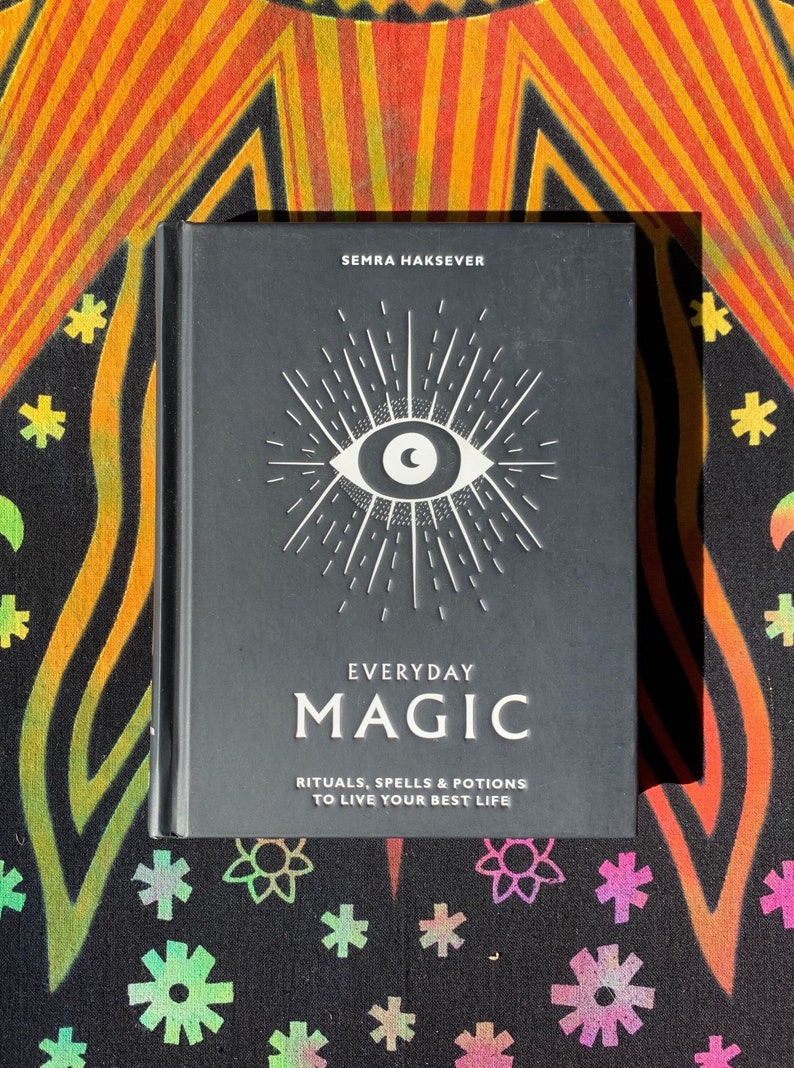 May include: A black book with a white eye and sunburst design on the cover. The title is "Everyday Magic: Rituals, Spells & Potions to Live Your Best Life".