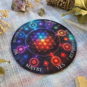 May include: A round divination board with a dark background and colorful geometric patterns. The board features the words "Yes," "No," "Maybe," and "Rephrase" around the edge. The center has a vibrant, multi-colored design.