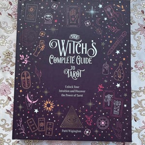 May include: A hardcover book titled "The Witch's Complete Guide to Tarot" with a dark purple cover. The cover features illustrations of tarot cards, stars, and other mystical symbols. The book's title and author's name are in white.