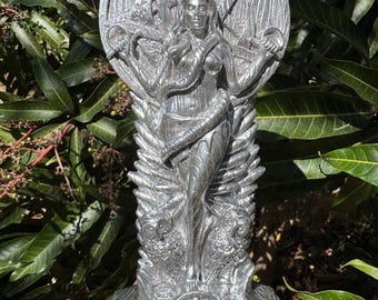 May include: A silver metal statue of a woman holding two swords, with a snake wrapped around her waist. The statue is standing on a base with a circular design.