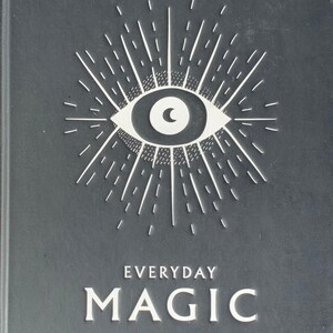 May include: A black book cover featuring a white eye and sunburst design. The title "EVERYDAY MAGIC" is printed in white, along with the text "RITUALS, SPELLS & POTIONS TO LIVE YOUR BEST LIFE".