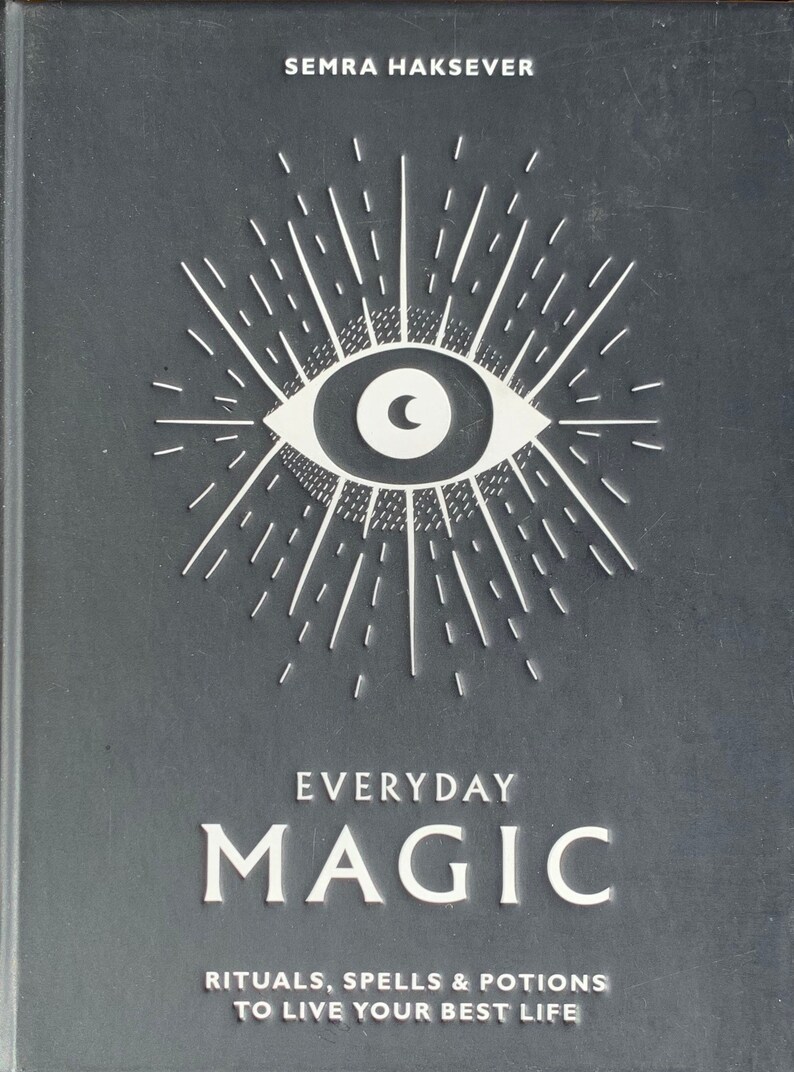 May include: A black book cover featuring a white eye and sunburst design. The title "EVERYDAY MAGIC" is printed in white, along with the text "RITUALS, SPELLS & POTIONS TO LIVE YOUR BEST LIFE".