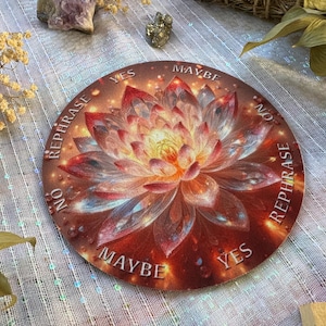 May include: A round divination board featuring a detailed lotus flower design in shades of red, orange, and yellow. The words "YES", "NO", "MAYBE", and "REPHRASE" are printed around the flower. The board has a slightly distressed, vintage look.
