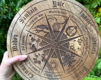May include: A wooden wheel with a star in the center and eight spokes. The wheel is divided into eight sections, each with a different symbol and text. The text includes the names of the eight sabbats: Samhain, Mabon, Lammas, Litha, Beltane, Imbolc, Yule, and Ostara.