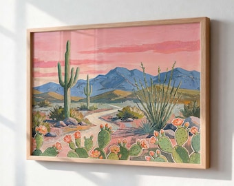 May include: A framed landscape painting depicting a desert scene with saguaro cacti, prickly pear cacti with orange blossoms, and a winding dirt path. The background features blue mountains under a soft pink and peach sunset sky in a wooden frame.