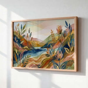 May include: A rectangular framed wall art print featuring a watercolor landscape with rolling hills in shades of ochre, blue, and pink. The foreground displays stylized botanical elements, including tall leaves and flowers in dark blue and gold tones.