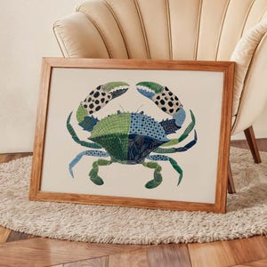 May include: A framed art print featuring a colorful crab illustration. The crab is depicted in shades of green, blue, and black, with intricate patterns on its shell and claws. The artwork is set against a cream-colored background and framed in natural wood.