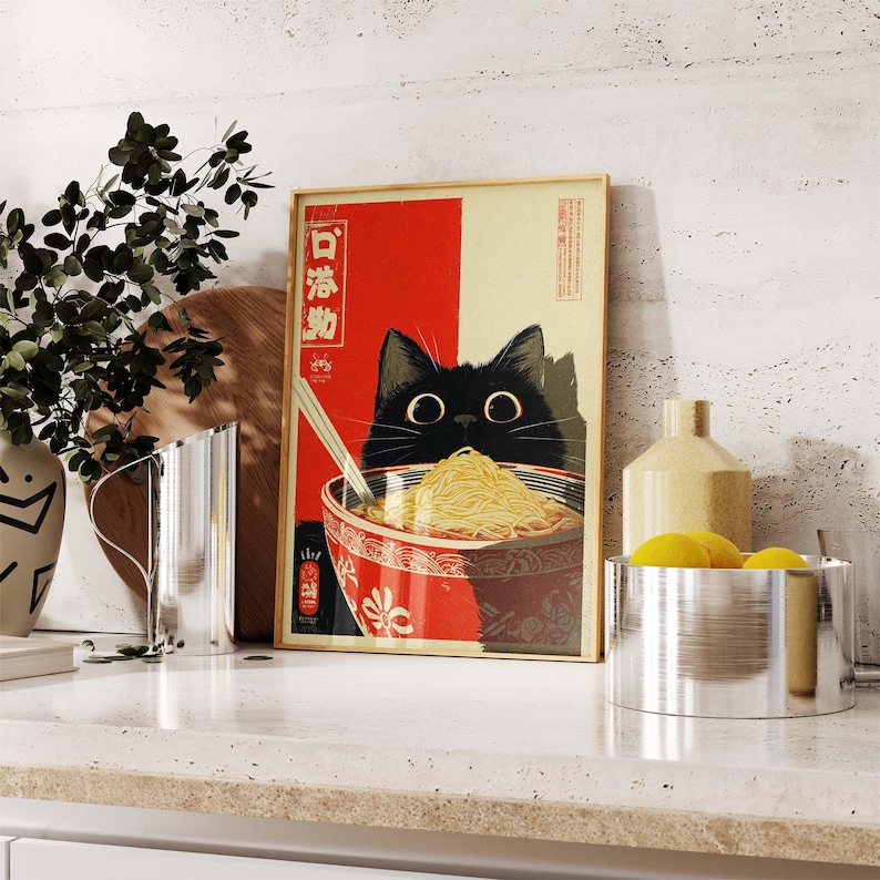 May include: A framed art print featuring a black cat peering over a bowl of ramen noodles. The artwork has a red and cream background with Japanese text. The cat has large, round eyes and is holding chopsticks.