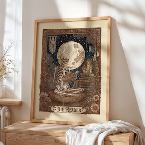 Op de afbeelding: Ingelijste kunstprint met een skelet dat een boek leest onder een volle maan. Het kunstwerk heeft een vintage stijl met gedetailleerde illustraties, kaarsen en de tekst "The Reader" onderaan. De lijst is van lichtkleurig hout.