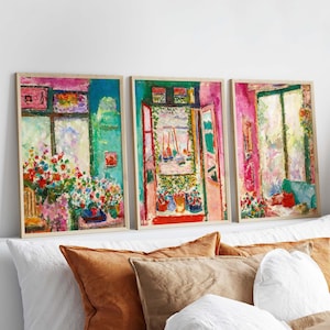 Puede incluir: Conjunto de tres impresiones artísticas enmarcadas que presentan pinturas impresionistas coloridas de ventanas y arreglos florales. La obra de arte muestra tonos vibrantes de rosa, verde, azul y rojo, con pinceladas visibles. Las impresiones se exhiben sobre una cama con almohadas.