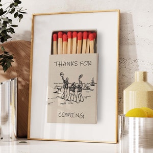 May include: A framed print of a matchbox with a drawing of three people in hats and the text "Thanks for coming".