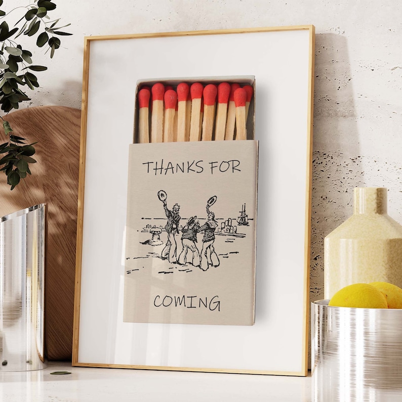 May include: A framed print of a matchbox with a drawing of three people in hats and the text "Thanks for coming".