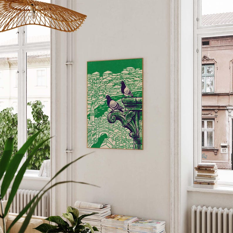 May include: A framed art print featuring a green and white illustration of a cityscape with two pigeons perched on a decorative ledge. The artwork has a vintage aesthetic, with a green background and a detailed depiction of buildings and architecture.