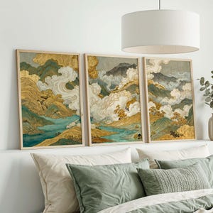 May include: A triptych of framed landscape prints depicting a mountain scene with gold, teal, and white hues. The artwork is displayed above a bed with green and white cushions, creating a tranquil and artistic bedroom setting.