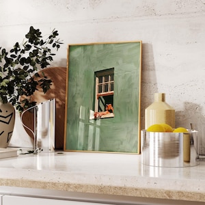 May include: A framed art print featuring a green wall with a window, depicting a person relaxing and reading. The artwork is displayed on a countertop with a vase, a decorative bottle, and a metal bowl with lemons.