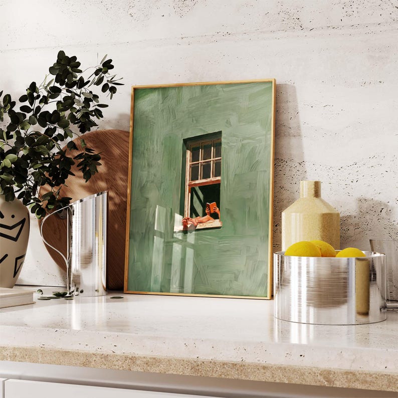 May include: A framed art print featuring a green wall with a window, depicting a person relaxing and reading. The artwork is displayed on a countertop with a vase, a decorative bottle, and a metal bowl with lemons.