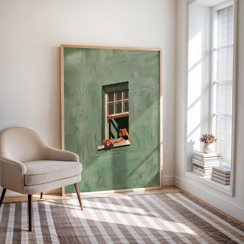 May include: A framed art print depicts a person reading a book in a window. The artwork features a green wall with a wooden window frame. The person's legs and the book are visible. A beige armchair and striped rug are in the foreground.
