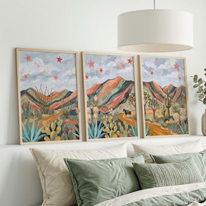 May include: Set of three framed landscape art prints. Each print features a colorful desert scene with mountains, cacti, and a winding road. The artwork includes a horse and rider, and red star accents against a blue sky.