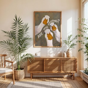 May include: A framed wall art print featuring three white ducks with orange beaks against a muted olive green background. The text "ARE YOU POOPING?" is written in white capital letters diagonally across the center of the artwork.