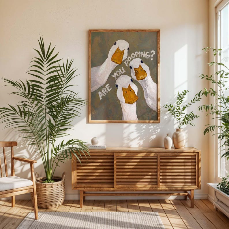 May include: A framed wall art print featuring three white ducks with orange beaks against a muted olive green background. The text "ARE YOU POOPING?" is written in white capital letters diagonally across the center of the artwork.