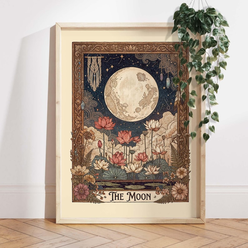May include: A framed art print depicting a full moon, lotus flowers, and a night sky. The illustration has a vintage style with a decorative border and the text "The Moon". The colour scheme includes blues, pinks, and browns. The frame is light-colored.