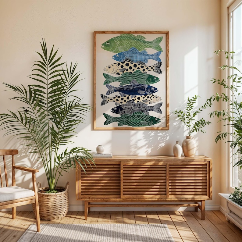 May include: A framed art print featuring a stack of stylized fish in shades of green, blue, and black. The fish have intricate patterns and are arranged vertically. The artwork is displayed on a light-colored wall above a wooden cabinet.