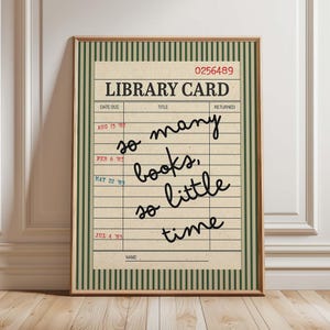 May include: A framed wall art print featuring a vintage library card design with a cream background, dark green vertical stripes, and the text "so many books, so little time" written in black script. Includes dates and the number 0256489.