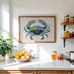 May include: A framed crab art print with a wooden frame. The crab is depicted in shades of green and blue, with patterned details. The artwork hangs on a white wall above a kitchen countertop. A bowl of lemons and jars of preserves are also visible.