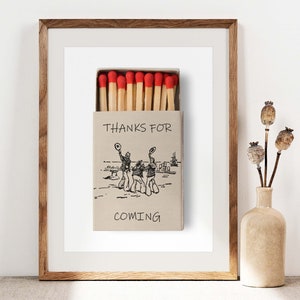 May include: A brown wooden frame with a white mount and a printed image of a matchbox with red match heads. The matchbox has the text "THANKS FOR COMING" printed on it.