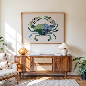 May include: A framed crab art print with a patchwork design in shades of green, blue, and black hangs above a wooden cabinet. The cabinet has a mid-century modern design with a light-colored woven panel and a white lamp.