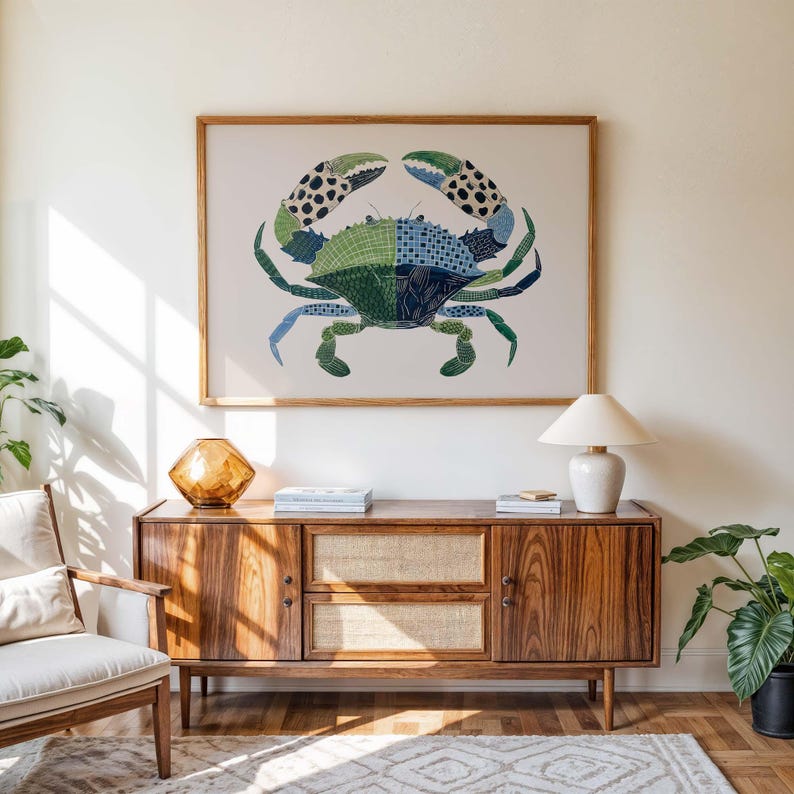 May include: A framed crab art print with a patchwork design in shades of green, blue, and black hangs above a wooden cabinet. The cabinet has a mid-century modern design with a light-colored woven panel and a white lamp.