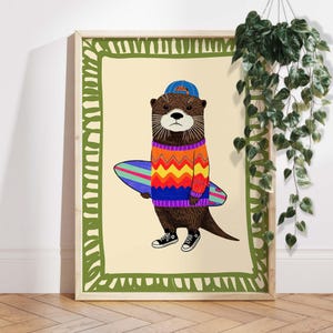 Peut inclure: Impression d'art encadrée représentant une loutre de dessin animé portant un pull coloré, une casquette bleue et des baskets noires, tenant une planche de surf. L'œuvre a une bordure vert clair et un fond crème.