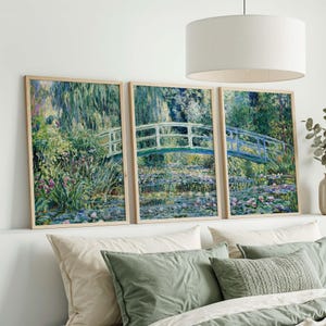May include: Three framed art prints showcasing a tranquil garden scene with a Japanese-style bridge over a pond with water lilies. The artwork uses greens, blues, and pinks, with a light wood frame. The prints are displayed above a bed with green and white pillows.